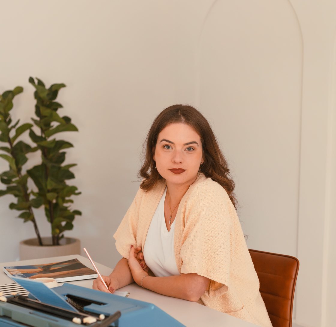Bruna Santanna sentada à mesa de trabalho, escrevendo ao lado de uma máquina de escrever azul